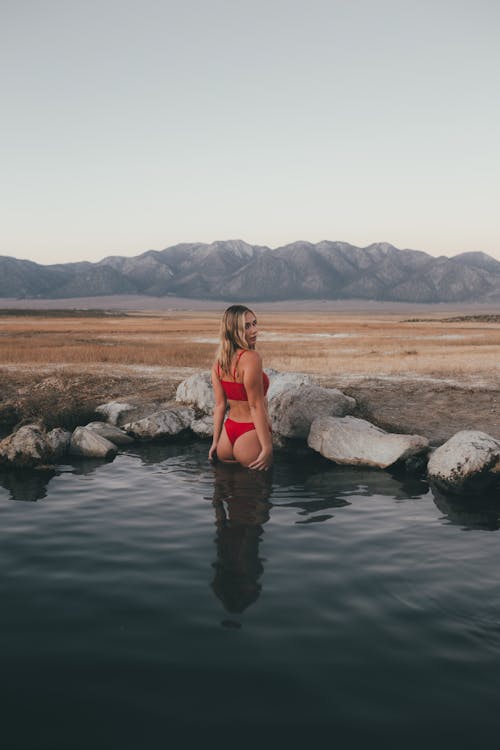 Woman in Red Bikini Sitting on Rock in the Middle of Lake