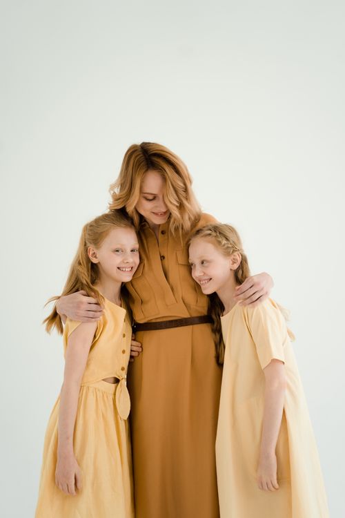 Free Mother joyfully embracing her twin daughters, showcasing family love and warmth. Stock Photo
