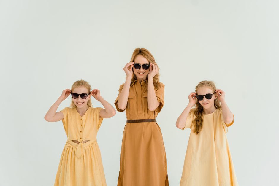 Stylish mother and daughters in matching dresses having fun indoors, wearing sunglasses