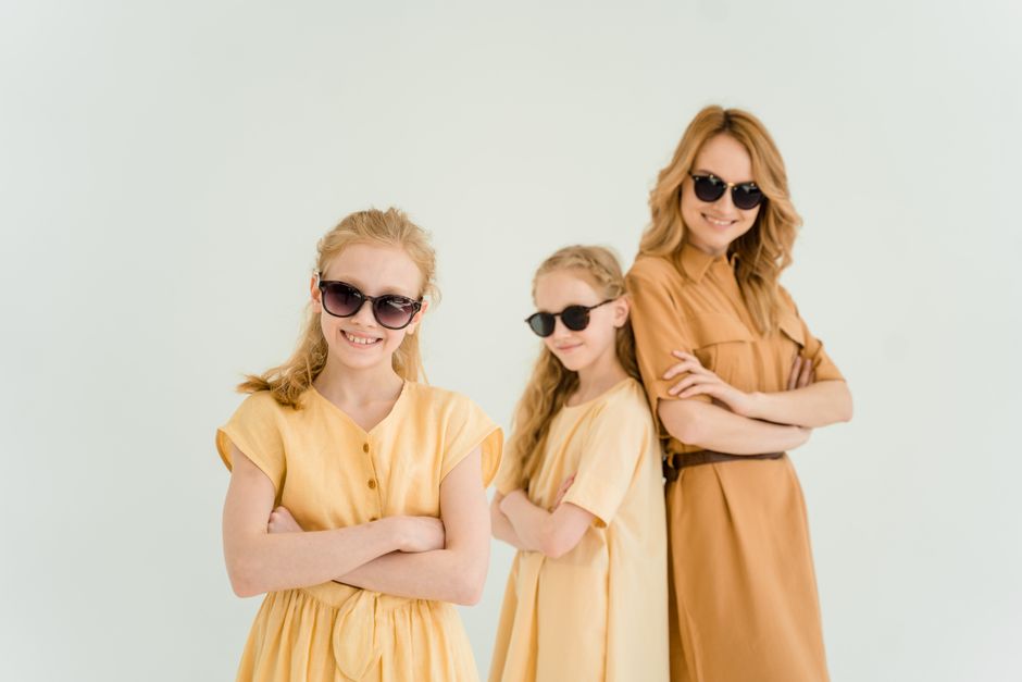 Happy family portrait with mother and daughters wearing sunglasses and yellow dresses in a studio setting.