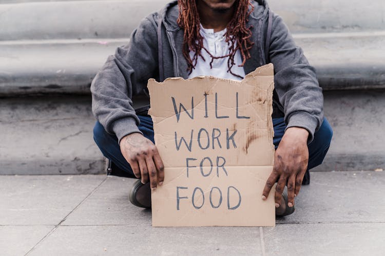 Man Holding A Cardboard Sign Sitting On A Floor