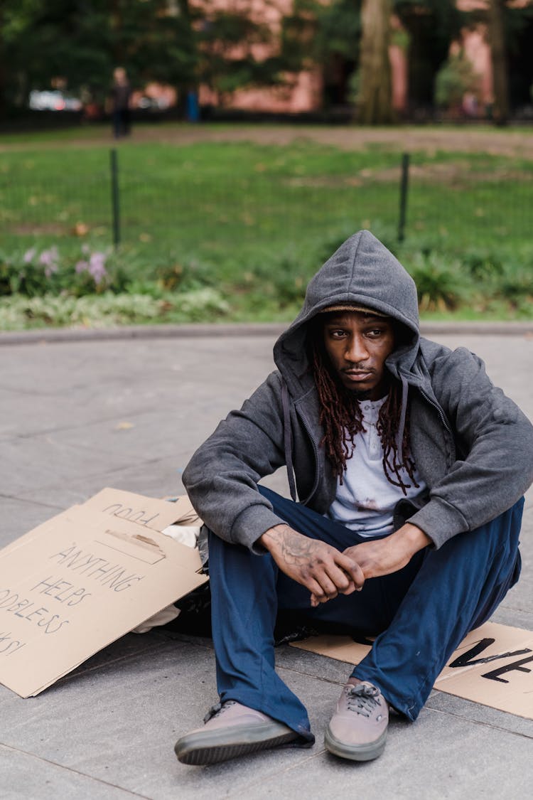 Man Sitting On The Street With Pieces On Cardboard 