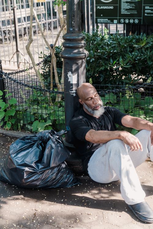 Free A homeless man in a black shirt rests against a lamp post in an outdoor setting. Stock Photo