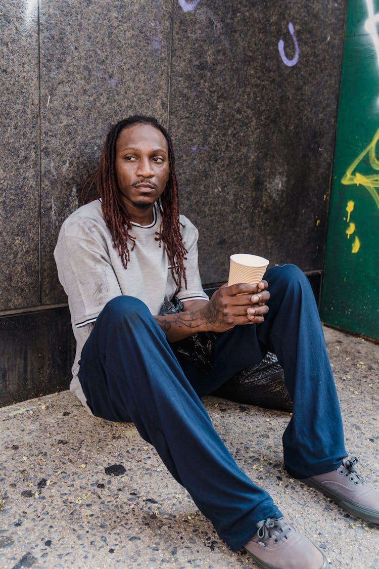 Man Sitting And Leaning On A Wall Holding A Paper Cup