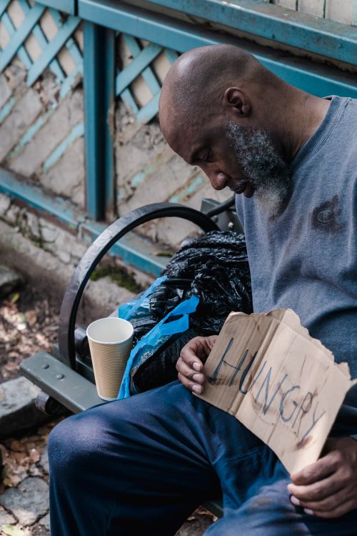 Free A poignant image of a homeless man on a bench holding a 'Hungry' sign, highlighting social issues. Stock Photo