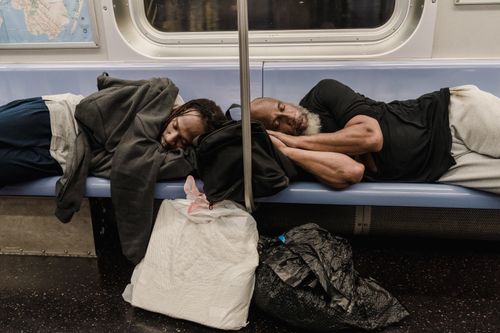 Free Two adults rest on a subway bench surrounded by bags, illustrating urban life. Stock Photo