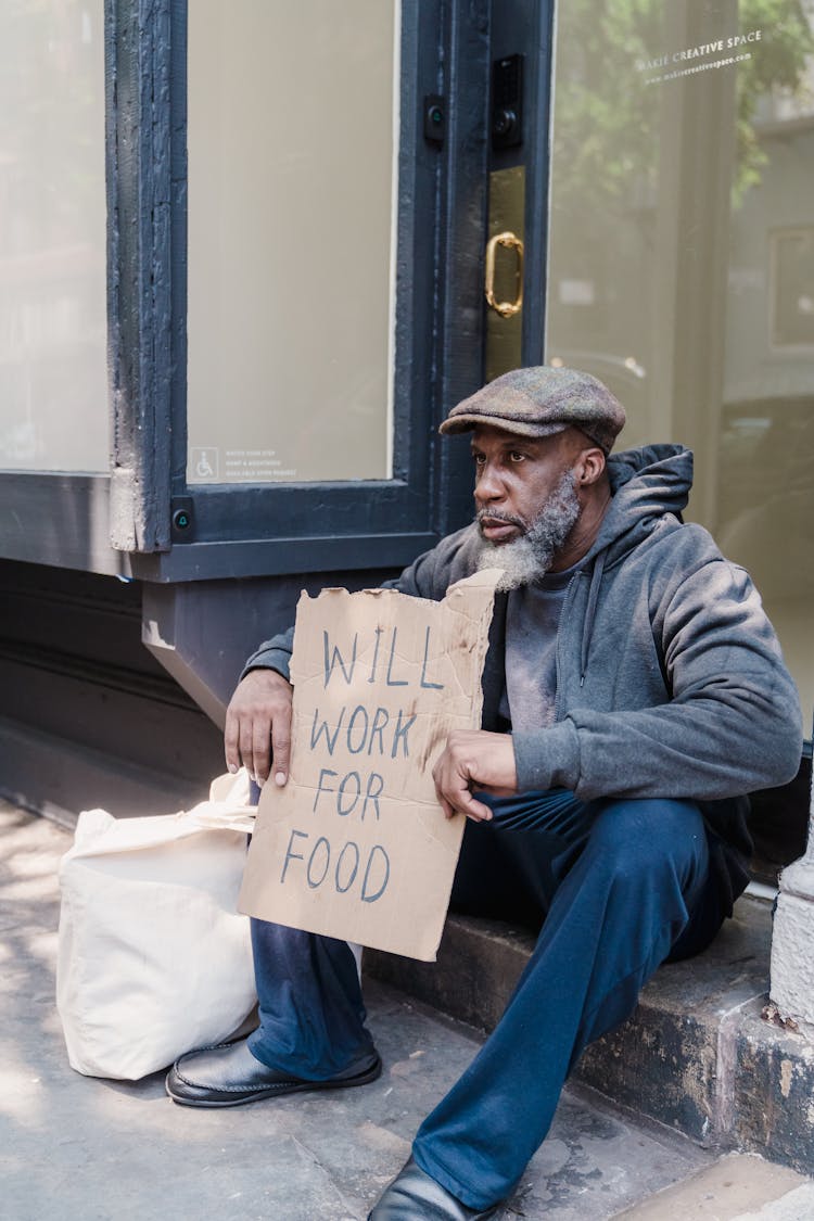 A Homeless Man Sitting With A Sign