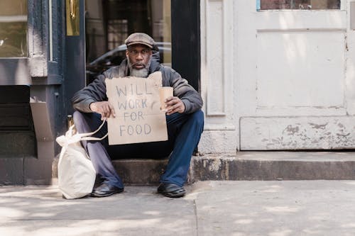 Free A Mature Man Sitting on the Doorway Holding a Cardboard a Sign Stock Photo