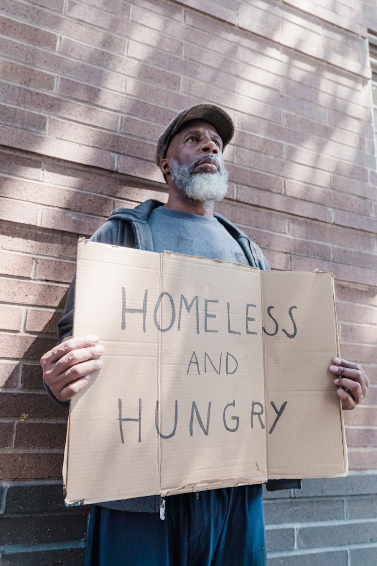 A Homeless Man Standing With A Sign