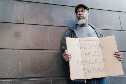 Free An Elderly Man Standing Beside a Wall Holding a Cardboard Sign Stock Photo