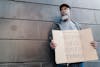 Free An Elderly Man Standing Beside a Wall Holding a Cardboard Sign Stock Photo