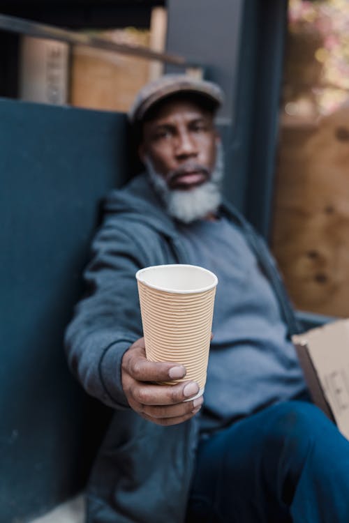 Selective Focus Photo of a Beggar Holding a Paper Cup