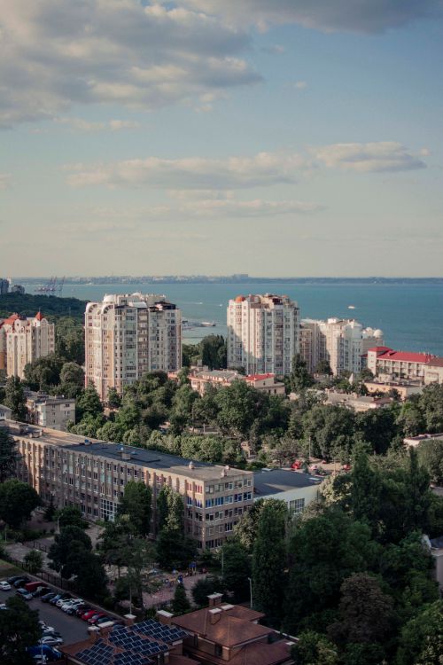 Free A picturesque aerial view showcasing tall buildings and lush greenery near a seaside, under a partly cloudy sky. Stock Photo