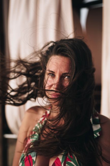 Close-up of a woman with long brown hair blowing in the wind, outdoors.