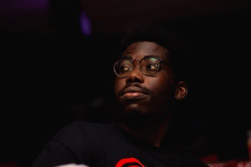 Close-Up Photo of a Man in a Black Shirt with Eyeglasses Looking Away