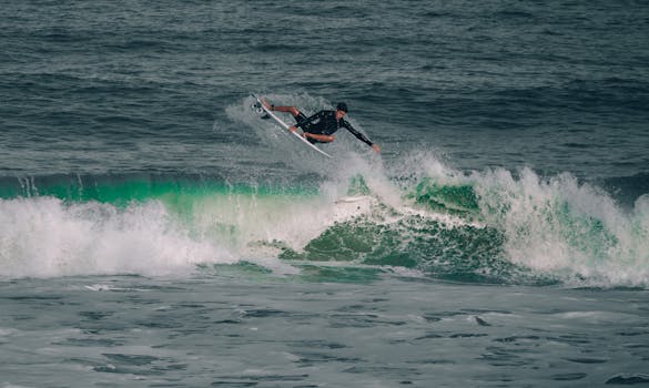 Surfer performing an aerial maneuver above the ocean wave, capturing motion and energy.