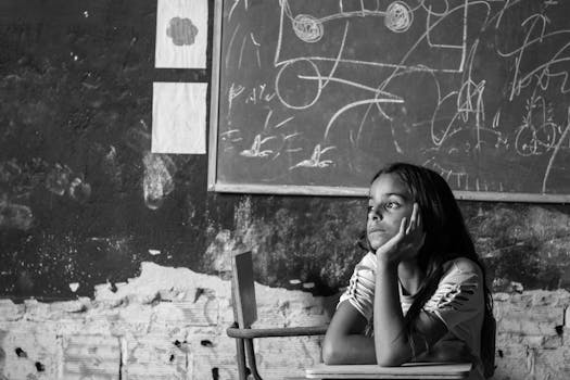 Black and white photo of a young girl sitting thoughtfully in a classroom in Bezerros, Brazil.