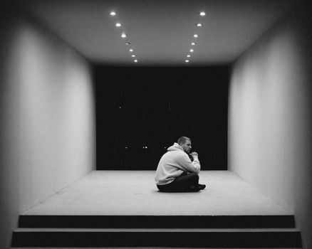 A man sits alone in a minimalist, monochromatic space, reflecting a sense of solitude.