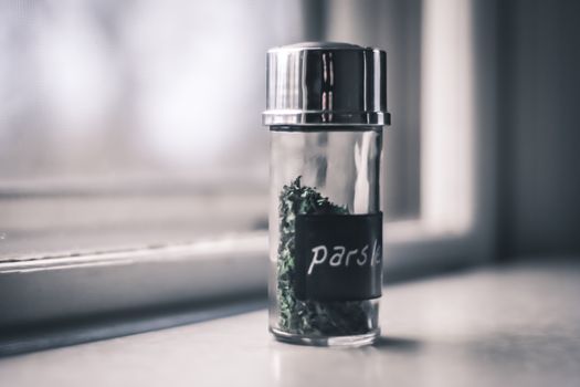 Close-up of a parsley herb shaker bottle on a windowsill indoors.