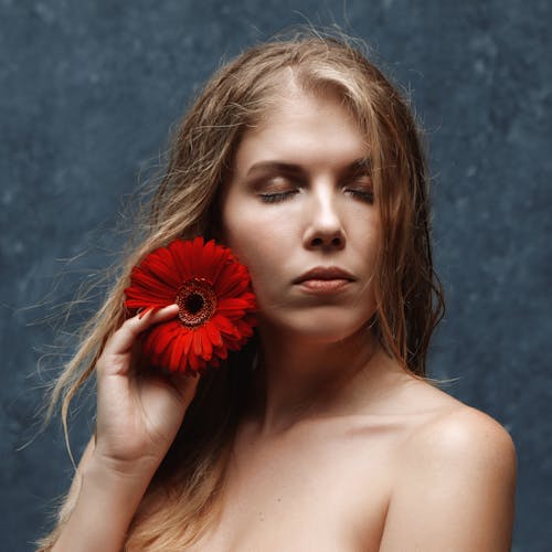 Close-Up Photo of a Woman Holding a Red Flower Beside Her Facew