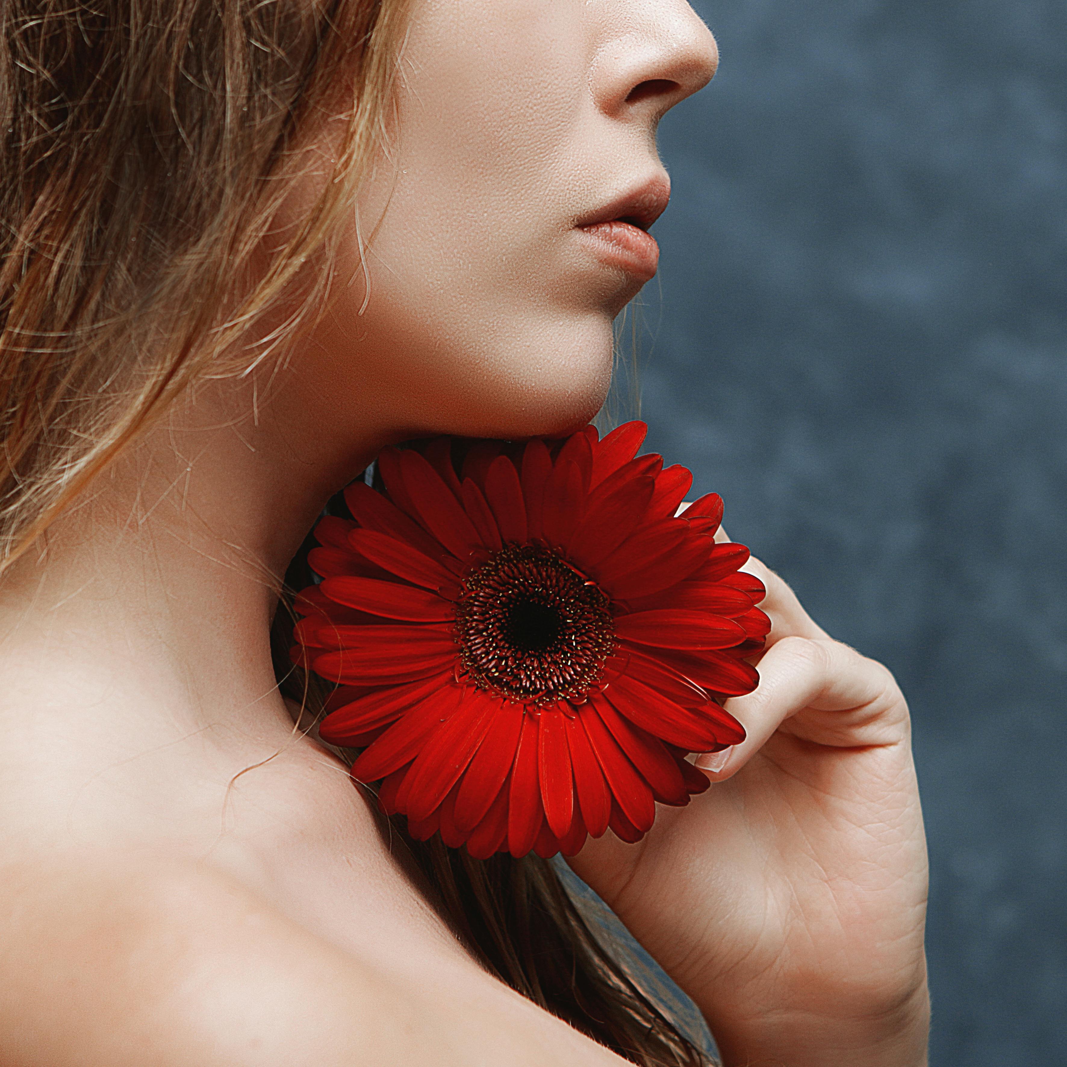 side view of a woman holding a red flower under her chin