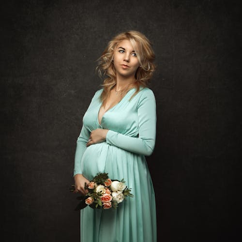 Photo of a Pregnant Woman in a Teal Dress Holding a Bouquet of Flowers