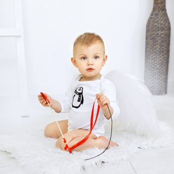 Cute baby sitting on a rug with ribbons, wearing angel wings, indoors.（イメージ）