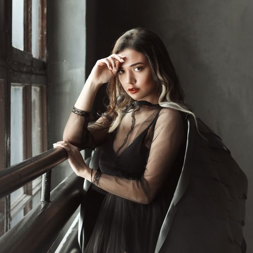 Free Stylish woman in sheer black dress poses thoughtfully by a window, exuding elegance. Stock Photo