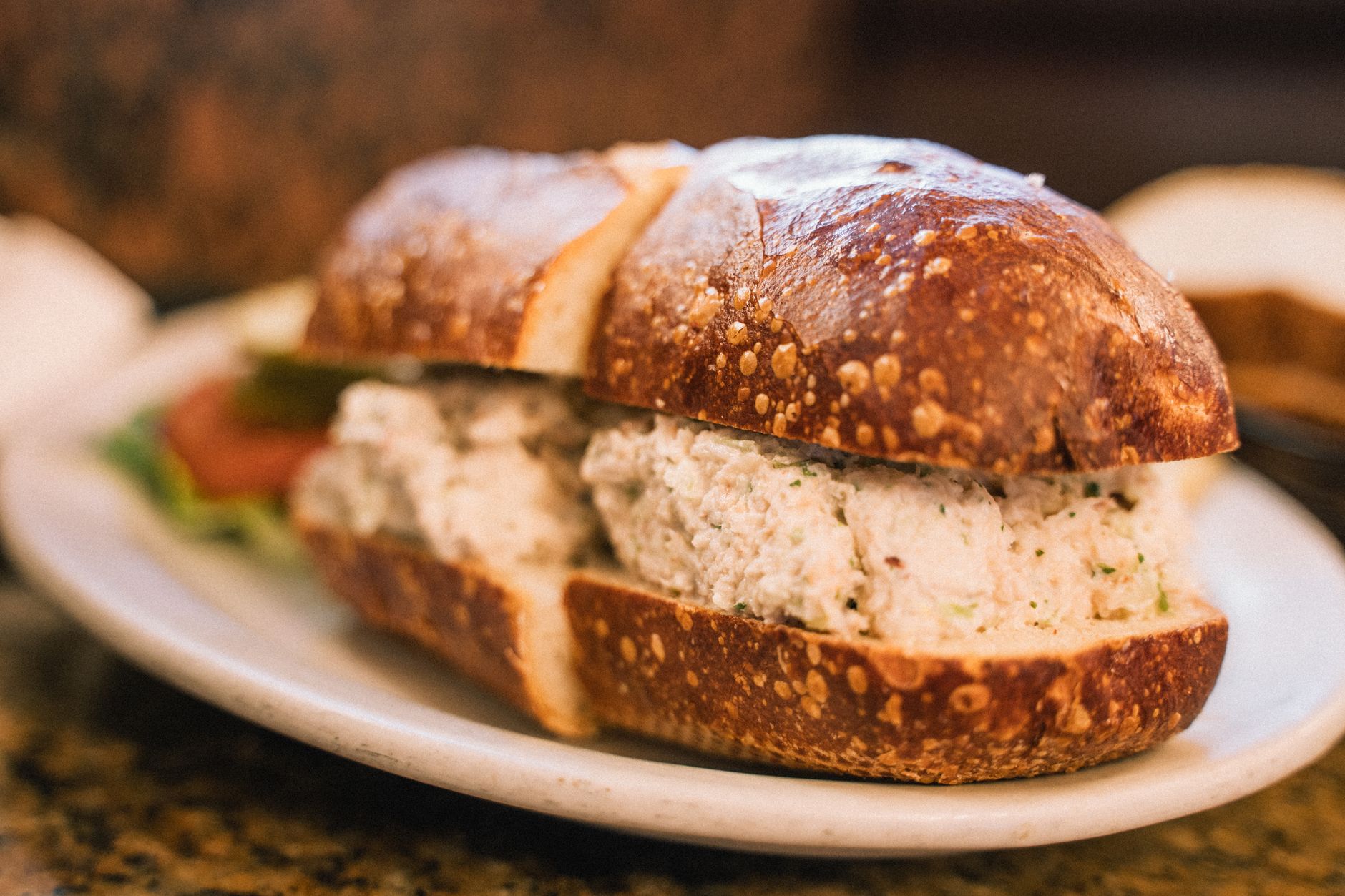 Fresh ingredients arranged on a wooden board including canned tuna, celery, herbs, and a baguette