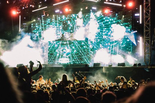 Vibrant music concert with DJ and crowd at night, showcasing lively atmosphere and dazzling lights.