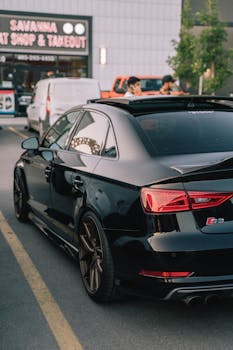 A shiny black sports car parked in an urban lot on a sunny day, showcasing modern automotive design.