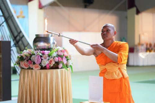 Free A Buddhist monk in orange robe performing a lighting ceremony indoors, signifying spiritual ritual. Stock Photo
