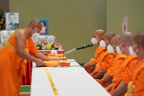 Men in Traditional Orange Robes Wearing Face Masks During a Ceremony