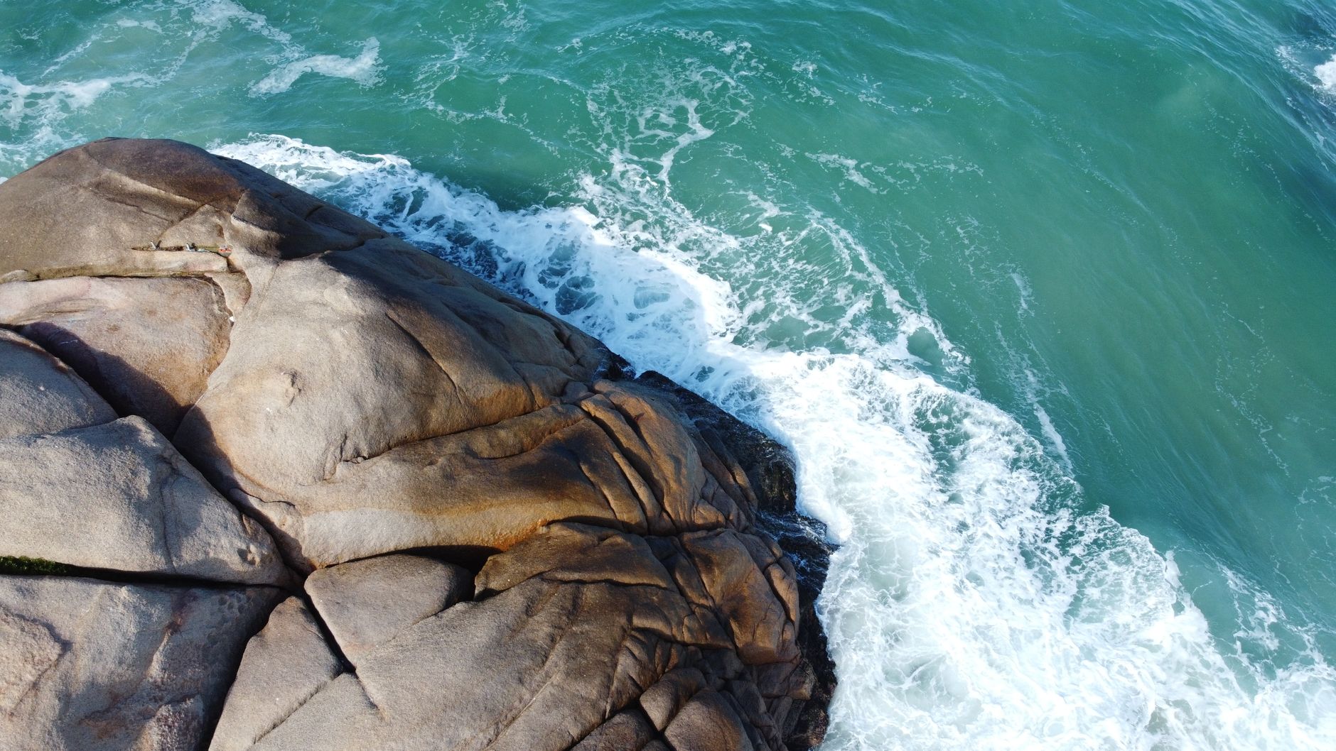 A stunning aerial view of ocean waves crashing against rocky cliffs in Santa Catarina, Brazil.