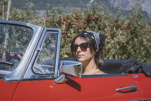 A Woman Wearing a Sunglasses and Bandana Driving a Red Car