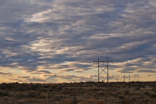 Free A striking view of power lines stretching across a field at sunset, with dramatic clouds enhancing the serene landscape. Stock Photo