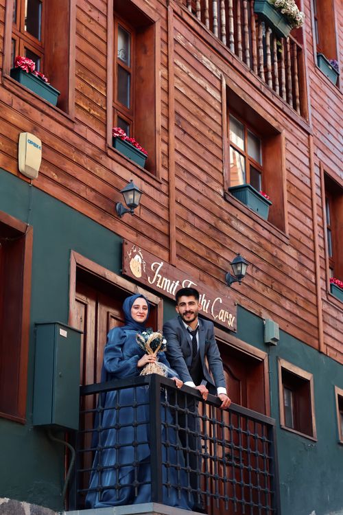 Free Elegant couple standing on a balcony of a rustic wooden building, smiling warmly. Stock Photo