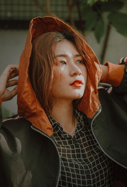 A fashionable young woman poses confidently outdoors in a stylish hooded jacket, capturing the sunlight.