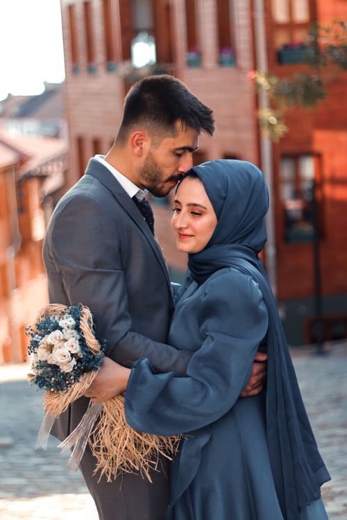 Free A couple embraces with a bouquet in a charming outdoor setting, exuding romance and love. Stock Photo