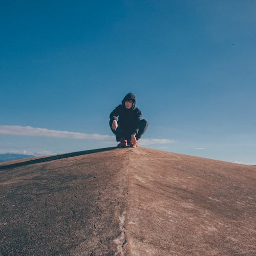 Free Man in Black Hoodie and Pants Sitting on Top of Rocky Cliff Stock Photo