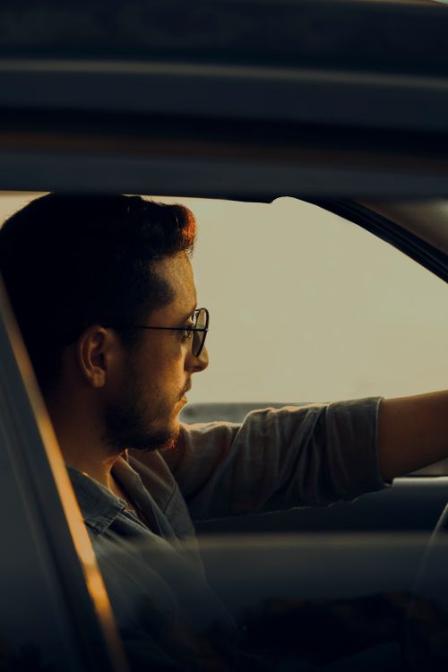 Free A man driving a car during sunset, showing a focused expression and wearing glasses. Stock Photo