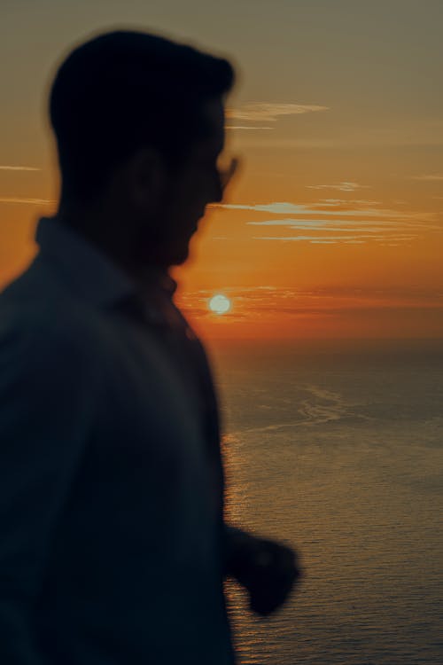 Silhouette of Man Standing Near the Sea during Sunset