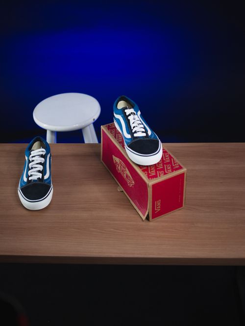 Free Blue sneakers displayed on a wooden surface with a branded box and white stool. Stock Photo