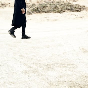 一个身穿黑色外套和靴子的人走过荒凉的沙漠，凸显出孤独感