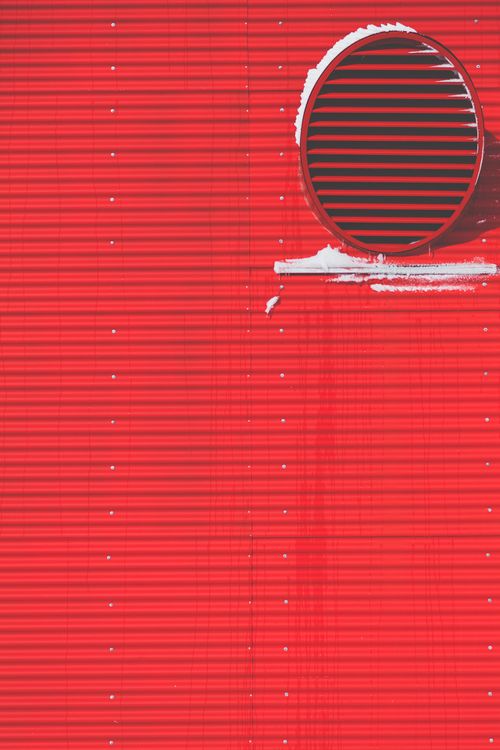 Free Close-up of a red corrugated metal wall featuring a circular ventilation grille. Stock Photo