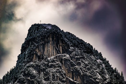 Snow-covered peak with cross, dramatic sky, Oberammergau, Germany.