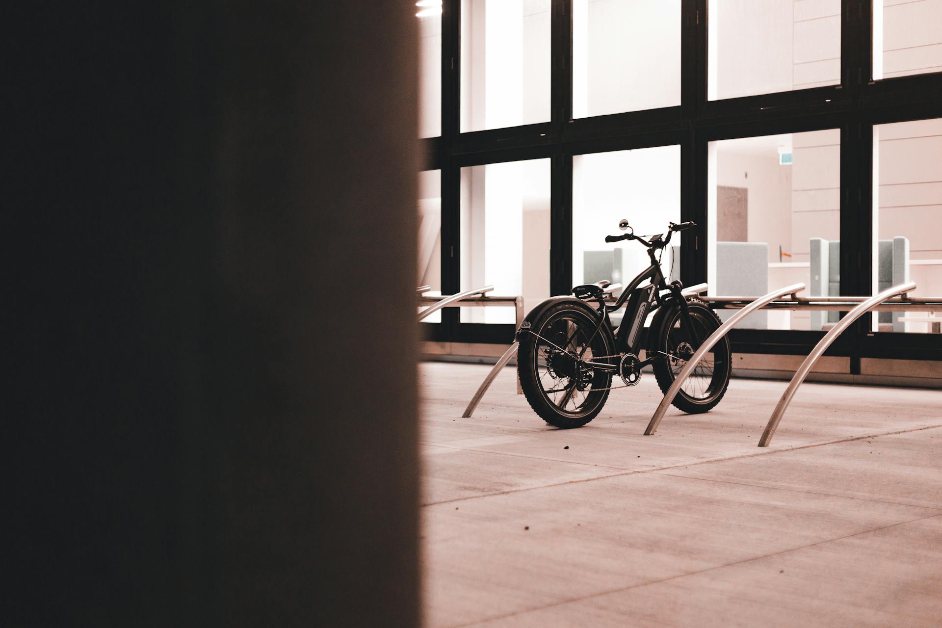 A modern electric bicycle parked indoors near a large glass wall with steel racks.