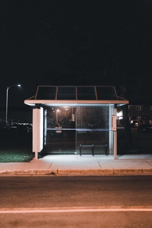 Free A street view of an illuminated bus stop at night showcasing urban public transport infrastructure. Stock Photo