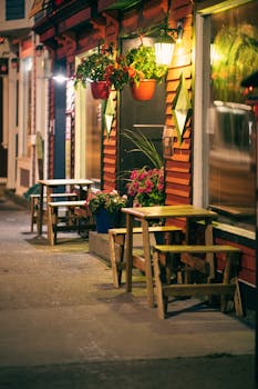 Cozy outdoor seating at a charming café illuminated at night with vibrant hanging flowers.
