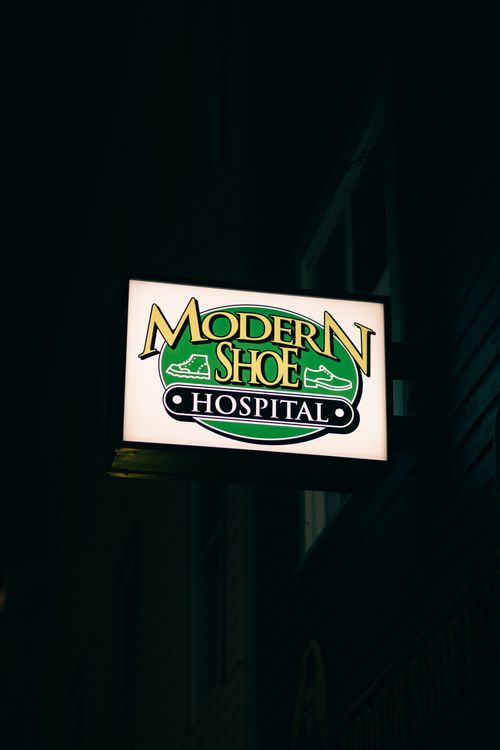 Free A glowing sign for Modern Shoe Hospital, captured in a dark, urban setting. Stock Photo